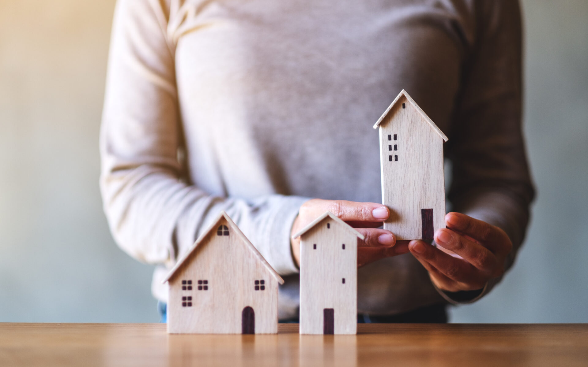 Closeup image of a woman holding wooden house models on the tabl